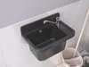 A black sink with a silver faucet is mounted on a tiled wall. A mop and bucket are visible to the right. Produktbild-Vorschau
