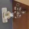 A close-up view of a cabinet hinge attached to a gray cabinet door and a brown wooden cabinet frame. Anteprima dell’immagine prodotto
