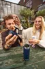 Two people sitting at a wooden table outdoors, holding and examining tea accessories. Podgląd zdjęcia produktu