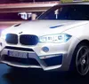 A white BMW car is driving at night, with its headlights on. Náhled obrázku produktu