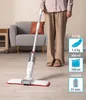 A person is using a white spray mop on a wooden floor in a room with a sofa and a side table. Produktbild-Vorschau