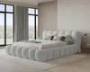 A modern bedroom with a large, upholstered bed as the focal point, featuring large windows with curtains and a view of greenery outside. Voir les images du produit