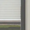 A close-up view of white pleated blinds covering a window, with a glimpse of the outdoors visible through the slats. Produktbild-Vorschau