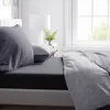 A neatly made bed with dark gray fitted sheet and light gray duvet cover, next to a window and a nightstand with a lamp and plant. Produktbild-Vorschau