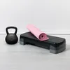 A black kettlebell and a pink yoga mat are placed on a black aerobic step, all on a light gray wooden floor against a white wall. Náhľad obrázku produktu