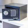 A small, dark gray safe with its door open, revealing a digital keypad and a dial, sits on a white shelf. Anteprima dell’immagine prodotto