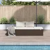 A brown poly rattan garden bed with white cushions is placed on a wooden deck next to a swimming pool, with a wooden fence and greenery in the background. Produktbild-Vorschau
