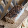 A loaf of bread with black seeds on top, placed on a wooden board. Produktbild-Vorschau