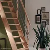 A wooden staircase with a metal railing is shown in a room with a green wall and a white wall decorated with framed pictures and a snake plant. Produktbild-Vorschau