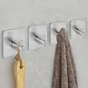 Four silver adhesive hooks are mounted on a light gray tiled wall. The leftmost hook has a wooden brush with a rope loop hanging from it. The second hook from the left has a brown and black patterned towel hanging from it. The third and fourth hooks are em Produktbild-Vorschau