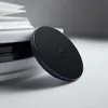 A black wireless charger is placed on a white surface next to a stack of books. Produktbild-Vorschau