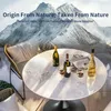 A round white table with bottles of wine and glasses on it, set against a backdrop of snowy mountains. Produktbild-Vorschau