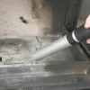 A hand is using a vacuum cleaner attachment to clean out a fireplace or wood stove. Produktbild-Vorschau