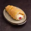 A single cream horn pastry filled with cream and cherries, placed on a textured plate. Podgląd zdjęcia produktu