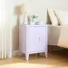 A purple nightstand with a door and handle, placed next to a bed with pillows. A lamp and some decorative items are on top of the nightstand. Náhľad obrázku produktu