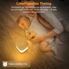 A baby sleeping next to a night light on a bed. Produktbild-Vorschau