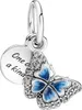 A close-up studio shot of a silver charm with a blue butterfly and a round disc. Produktbild-Vorschau