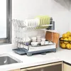 A two-tier dish drying rack filled with dishes, glasses, and bowls, placed on a kitchen countertop next to a sink. Podgląd zdjęcia produktu