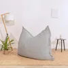 A light gray striped beanbag chair is placed on a beige rug in a minimalist room with a floor lamp and a small side table. Voir les images du produit