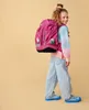 A young girl wearing a backpack and casual clothing, posing against a plain background. Náhled obrázku produktu