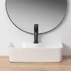 A white rectangular vessel sink with a black faucet is shown in front of a large round mirror against a white wall. Anteprima dell’immagine prodotto