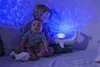 Two children are sitting on a bed with a whale-shaped night light projecting a blue ocean wave pattern on the wall. Anteprima dell’immagine prodotto