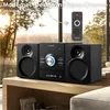 A stereo system with speakers and a remote control is displayed on a wooden table in front of a window with trees and sunlight. Produktbild-Vorschau