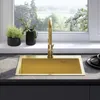 A gold sink with a gold faucet is shown in a kitchen setting, with plants on the windowsill and a view of greenery outside. Podgląd zdjęcia produktu