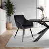 A black velvet dining chair is placed on a light gray rug next to a wooden dining table in a well-lit room. Náhled obrázku produktu