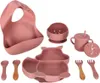 A set of silicone baby feeding items, including a bib, bowls, a cup with a straw, a plate, and utensils, arranged on a white background. Voir les images du produit