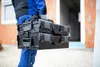 A person in work clothes carrying two black toolboxes. Produktbild-Vorschau