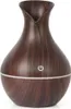 A dark brown, wood-grain patterned aroma diffuser with a white power button symbol and a white light strip around the base. Produktbild-Vorschau