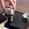 A hand is using a coffee distributor on a portafilter filled with coffee grounds, placed on a black mat. Náhľad obrázku produktu