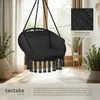 A black hanging chair with tassels is shown indoors, near a window with sheer curtains. Plants and a woven basket are also visible. Náhled obrázku produktu