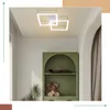 A modern white ceiling lamp with two interlocking square frames is shown installed on a white ceiling. Below the lamp, a green arched shelf unit displays a model boat and a teddy bear. Produktbild-Vorschau