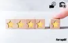 A hand is placing a wooden block with a star on it next to other blocks with stars, suggesting a rating or review system. Icons representing money, a thumbs-up, and a warehouse with a checkmark are in the upper right corner. Produktbild-Vorschau