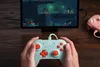 Hands holding a mint green game controller in front of a tablet displaying a video game. Produktbild-Vorschau
