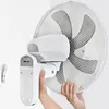 Hands are shown attaching a white wall-mounted fan to its bracket on a white wall. Podgląd zdjęcia produktu
