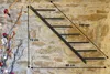 A metal wine rack mounted on a stone wall, with dimensions indicated by measurement lines and text. Podgląd zdjęcia produktu
