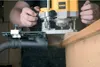 A person is using a DeWALT router with a dust collection attachment on a piece of wood. Produktbild-Vorschau
