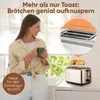 A woman holding a mug in a kitchen, with a toaster and bread rolls in the foreground. Produktbild-Vorschau