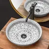 A close-up shot of a decorative washbasin with a black faucet, placed on a wooden countertop. Produktbild-Vorschau