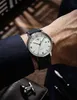 A person wearing a watch and suit, with cufflinks and pens in the foreground. Voir les images du produit