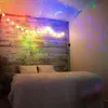 A bedroom with a projector displaying stars and a moon on the ceiling and walls, with string lights on a wooden wall above a bed. Produktbild-Vorschau