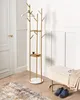 A gold and white coat rack with marble shelves stands in a hallway next to a door and a bench with shoes. Náhled obrázku produktu