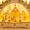 A wooden Christmas decoration with LED candles, depicting a winter scene with a church, houses, and carolers. Produktbild-Vorschau