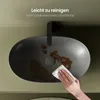 A hand is cleaning a dirty oval sink with a white cloth. Text overlays indicate the sink is easy to clean and has a dirt-repellent surface. Produktbild-Vorschau