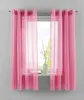 A window with pink curtains and sheer overlays, with a white vase and decorative branches on the windowsill.