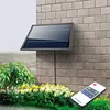 A solar panel is mounted on a brick wall above a flower bed, with a remote control in the foreground. Podgląd zdjęcia produktu