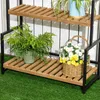A three-tiered plant stand with plants and flowers on it, set against a white slatted background and green artificial grass. Produktbild-Vorschau